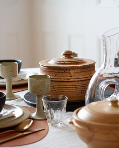 Dinner table setting with vintage ceramic, leather, brass, copper, and wooden tableware and glassware on a neutral background. All vintage items curated by Parliament Interiors in Vancouver, BC.