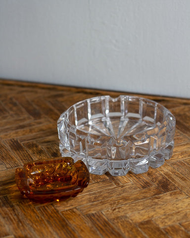 Vintage clear glass ashtray and amber glass dish on a vintage chevron-patterned wooden side-table with a neutral white background wall. All items curated by Parliament Interiors in Vancouver, BC.